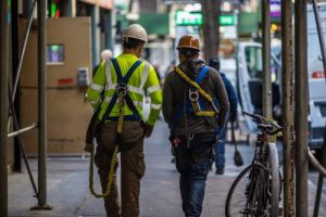 Two construction workers walk together down a sidewalk