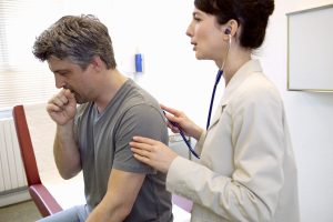Doctor using Stethoscope to examine man's lungs as he coughs